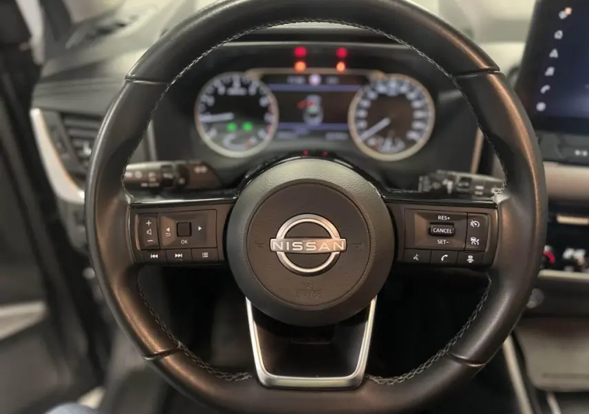 Volant cuir noir du Nissan Qashqai 1.3 Mild Hybrid 2023 avec commandes intégrées et tableau de bord numérique flou.