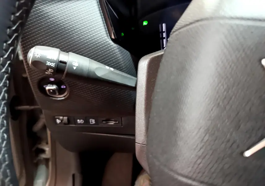 Détail du commodo d'éclairage à gauche du volant cuir dans l'habitacle sombre d'une DS4 E-TENSE 225 TROCADERO.