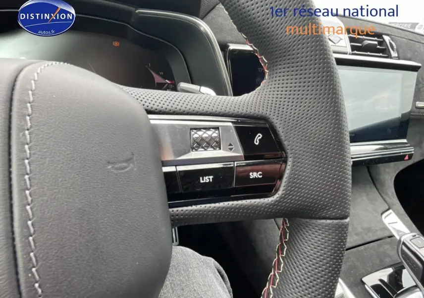 Gros plan sur le volant en cuir perforé avec commandes intégrées du DS7 gris titane, tableau de bord et écran tactile visibles.