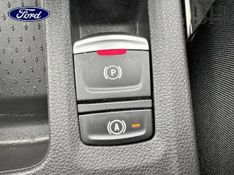 Gros plan sur les commandes de frein de stationnement et d'arrêt automatique sur console noire intérieure.