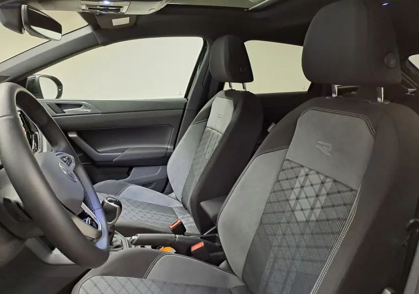 Vue intérieure côté conducteur du Volkswagen Taigo 1.5 TSI R-Line, sièges sport en tissu gris avec logo R brodé.