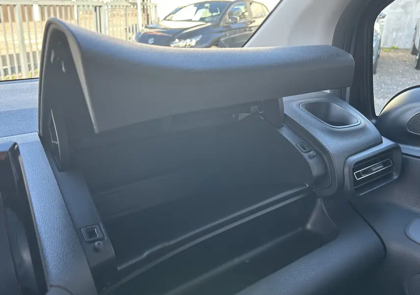 Vue intérieure du Peugeot Partner Fourgon 2026 montrant la boîte à gants ouverte côté passager, tableau de bord noir.