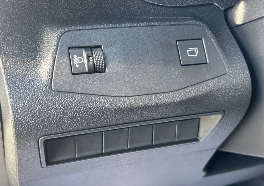 Gros plan sur les commandes de réglage des phares et du tableau de bord noir du Peugeot Partner Fourgon gris acier.