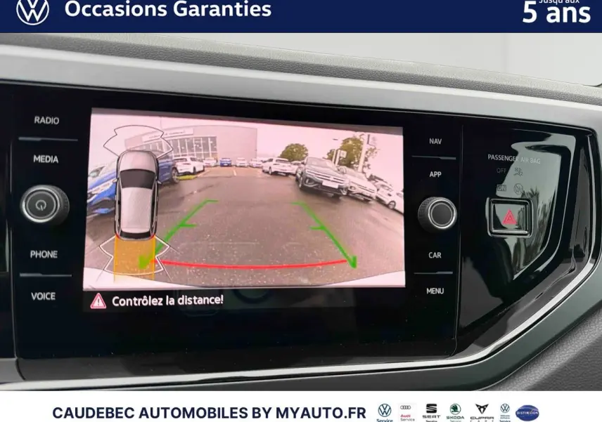 Écran tactile intérieur affichant la caméra de recul d'une Volkswagen Polo blanche, vue arrière avec aides au stationnement.