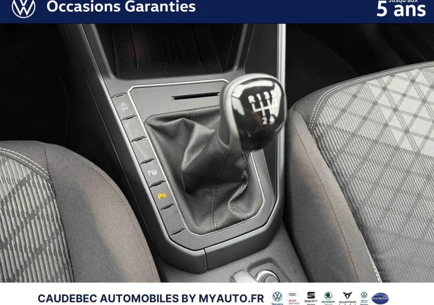 Gros plan sur la commande de boîte manuelle et les sièges gris à motifs de la Volkswagen Polo blanche.