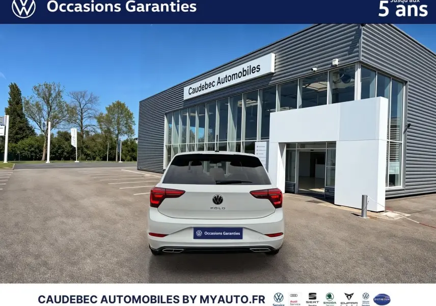 Vue arrière d'une Volkswagen Polo blanche 2025 garée devant un bâtiment moderne de concession automobile.