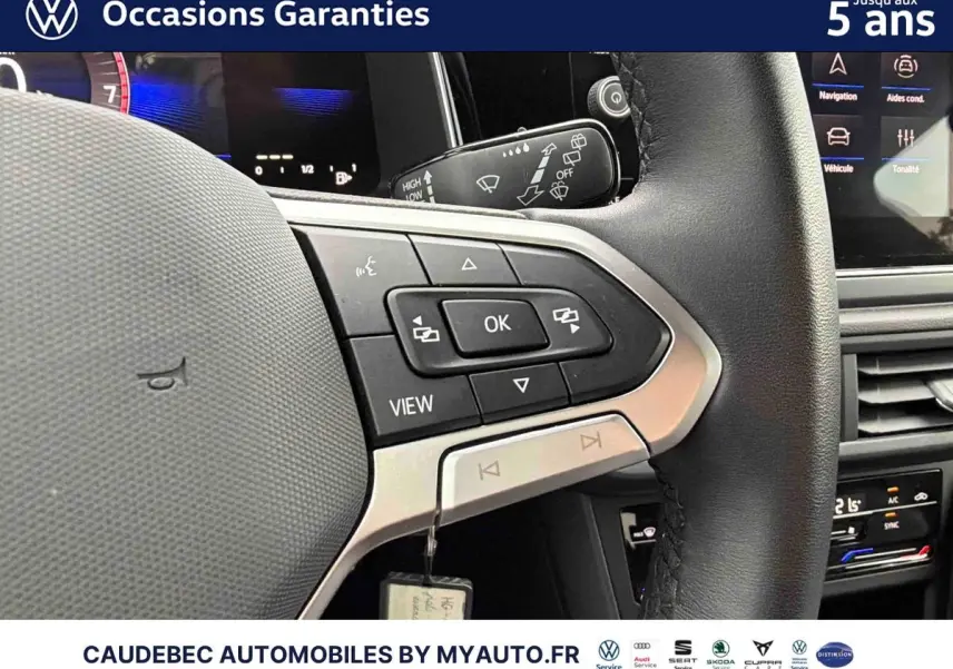 Gros plan sur le volant cuir multifonctions noir de la Volkswagen Polo 2025 avec commandes intégrées et tableau de bord digital en arrière-plan.