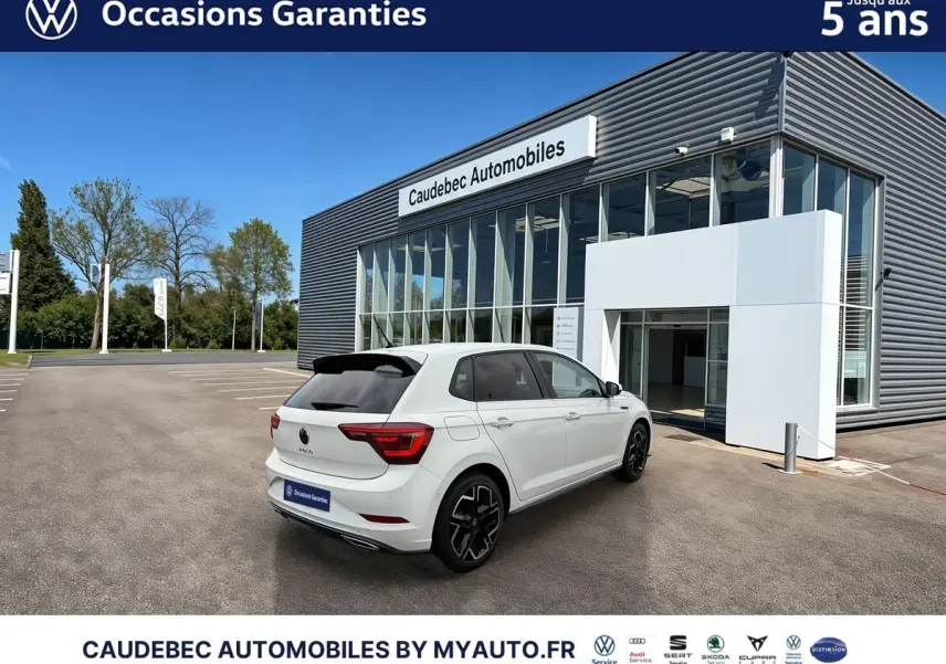 Vue 3/4 arrière droite d'une Volkswagen Polo blanche avec jantes alliage 17" devant un bâtiment Caudebec Automobiles.