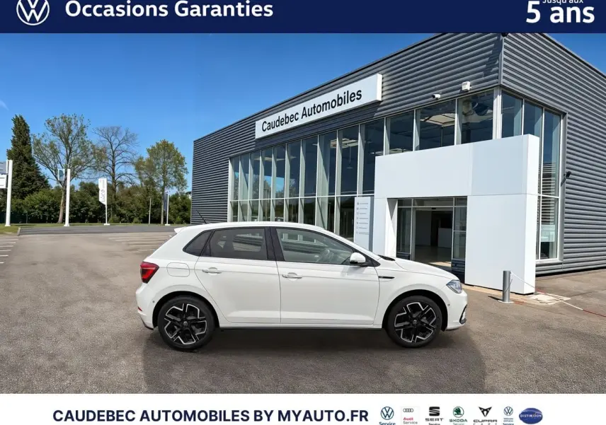 Profil droit d'une Volkswagen Polo blanche 2025 avec jantes alliage 17 pouces, devant un bâtiment Caudebec Automobiles.