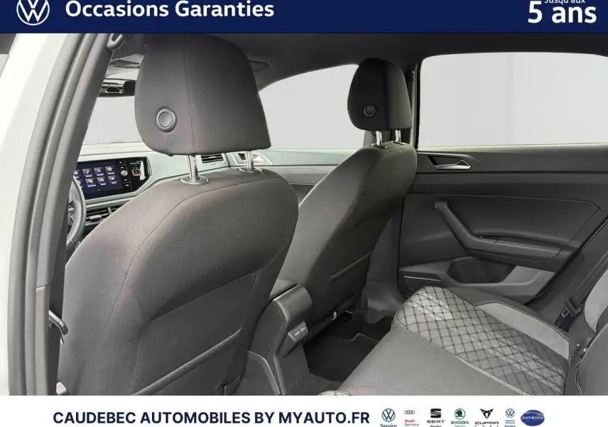 Vue intérieure arrière de la Volkswagen Polo blanche 2025, montrant les sièges avant et arrière en tissu gris avec motifs.