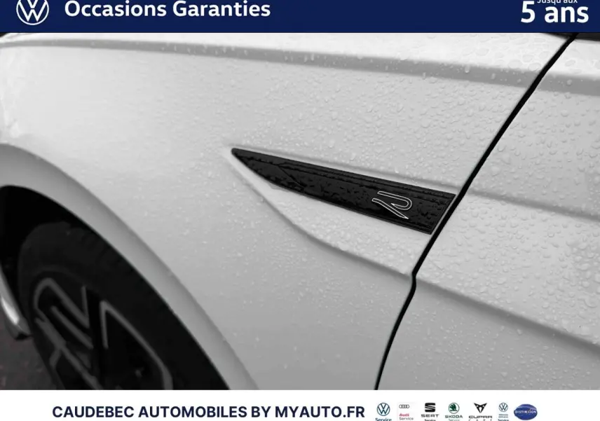 Détail du logo R sur l'aile avant gauche d'une Volkswagen Polo blanche avec gouttes d'eau visibles.