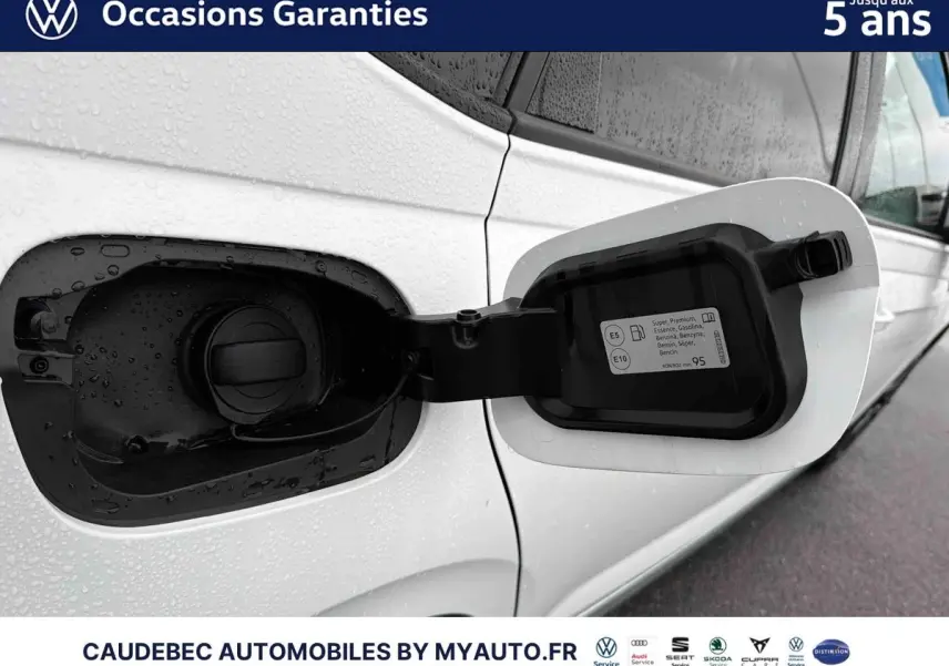 Vue rapprochée de la trappe à carburant côté gauche d’une Volkswagen Polo blanche avec étiquette essence visible.
