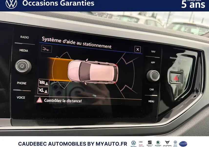 Écran tactile intérieur de la Volkswagen Polo 2025 montrant l’aide au stationnement avec vue du dessus du véhicule blanc.