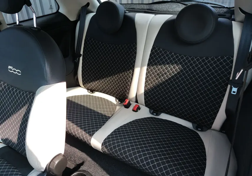 Vue intérieure arrière de la Fiat 500 blanche, sièges en tissu noir à motif quadrillé avec surpiqûres blanches et appuie-têtes ronds.