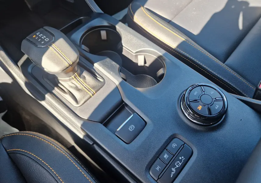 Gros plan sur la console centrale du Ford Ranger Wildtrak gris, avec levier de vitesse, sélecteur 4x4 et coutures orange sur cuir noir.