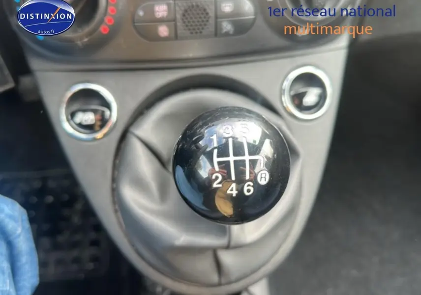 Gros plan sur le levier de vitesses manuel noir de la FIAT 500 gris, avec les commandes de climatisation en arrière-plan.