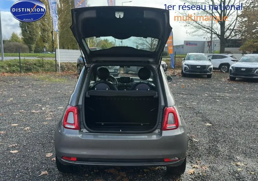 Vue arrière d'une FIAT 500 gris avec coffre ouvert, montrant l'intérieur et les sièges avant dans un parking extérieur.