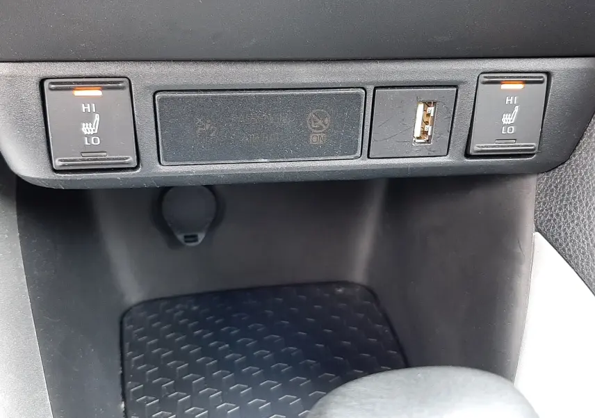 Gros plan sur les commandes de sièges chauffants et prise USB dans une Toyota Yaris blanche 2023, intérieur noir.