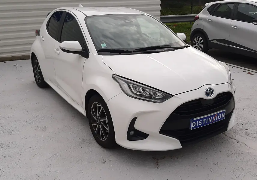 Toyota Yaris blanche vue 3/4 avant droit, avec calandre noire et jantes alliage bicolores.