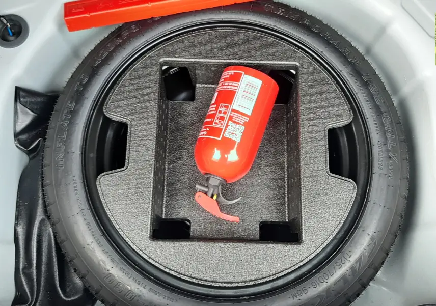 Vue plongeante sur la roue de secours et l'extincteur rouge dans le coffre d'une Toyota Yaris blanche 2023.