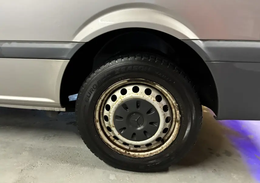 Gros plan sur la roue arrière droite grise d’un Mercedes Vito 2.8 113 CDI Fourgon Long avec jante acier et logo Mercedes central.