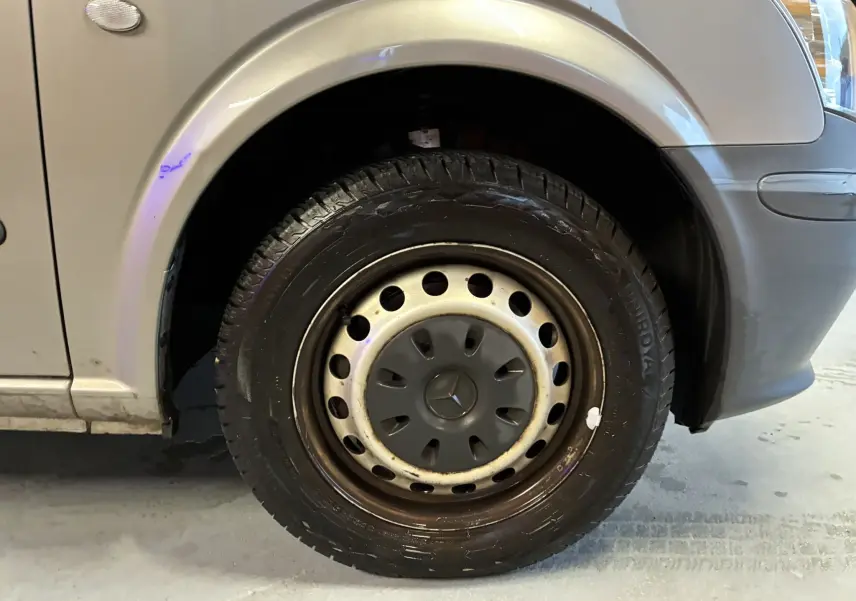 Gros plan sur la roue avant gauche grise d’un Mercedes Vito 2.8 113 CDI Fourgon Long de 2012, avec jante acier et logo Mercedes.