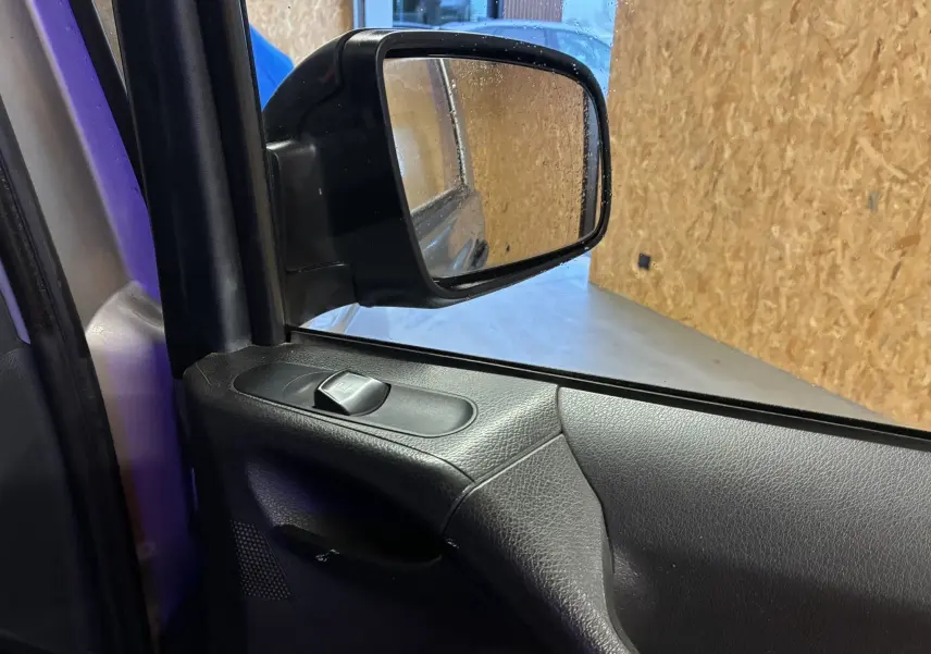 Vue intérieure sur le rétroviseur côté gauche d’un Mercedes Vito gris 2012, avec commande de lève-vitre noire.