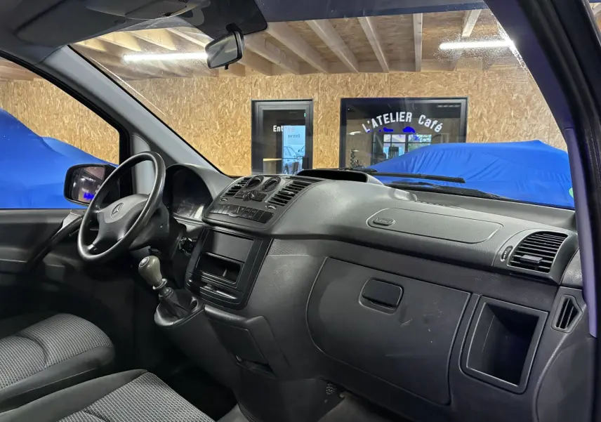 Vue intérieure côté conducteur du Mercedes Vito gris 2012, mettant en valeur le tableau de bord noir et la boîte manuelle.