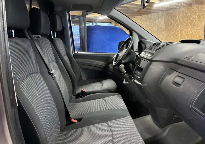 Vue intérieure côté conducteur du Mercedes Vito gris 2012, montrant les sièges tissu noirs et la console avec boîte manuelle.