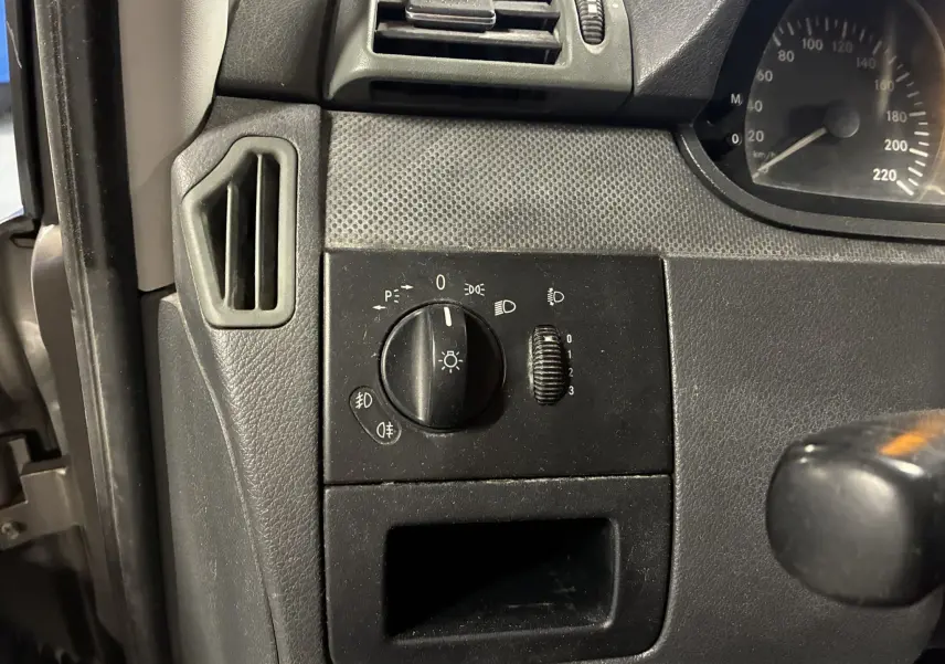 Détail du tableau de bord noir du Mercedes Vito 2.8 113 CDI gris, avec commande d’éclairage et aérateur côté gauche.