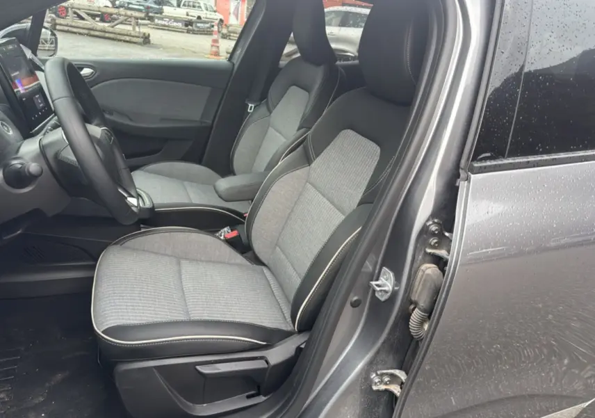 Vue intérieure côté conducteur de la Renault Clio gris schiste 2025, sièges tissu et cuir, tableau de bord avec écran tactile.