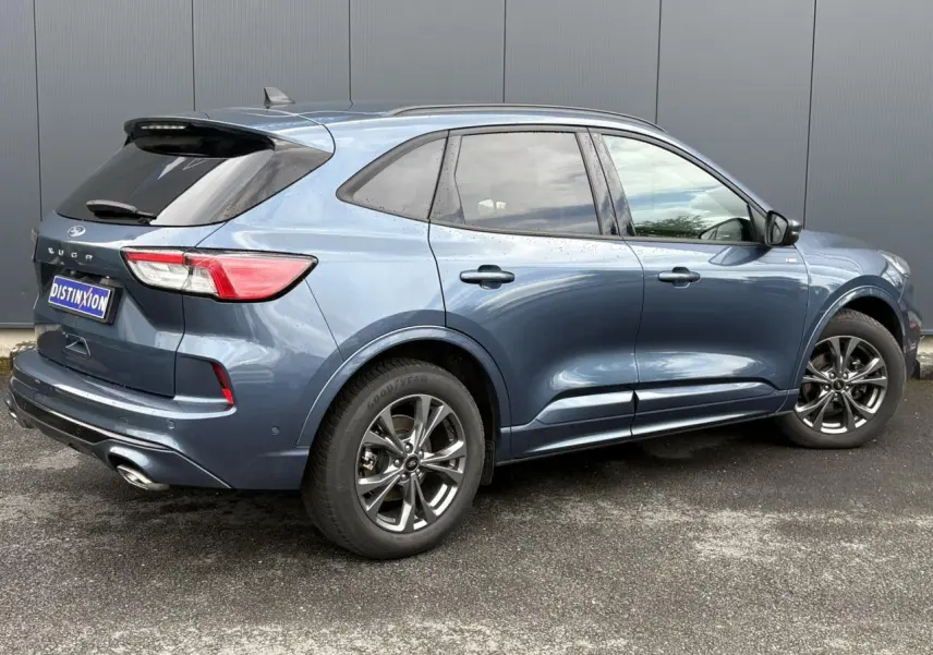 Vue 3/4 arrière droite d’un Ford Kuga 2023 bleu azur avec jantes alliage 18 pouces et double sortie d’échappement.
