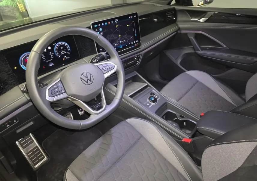 Vue intérieure côté conducteur du Volkswagen Tiguan 2025 noir, avec tableau de bord numérique et sièges tissu gris.