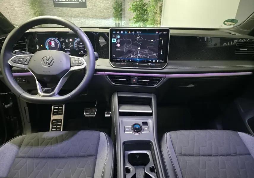 Vue intérieure avant du Volkswagen Tiguan noir 2025, tableau de bord numérique et écran tactile central avec navigation.