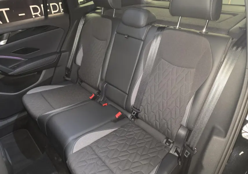 Vue intérieure de la banquette arrière noire et grise du Volkswagen Tiguan 2025 avec ceintures et appuie-têtes visibles.