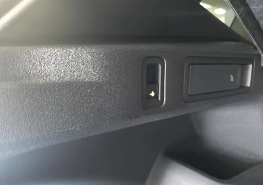 Détail du bouton d'ouverture électrique du hayon dans le coffre du Volkswagen Tiguan noir 2025.