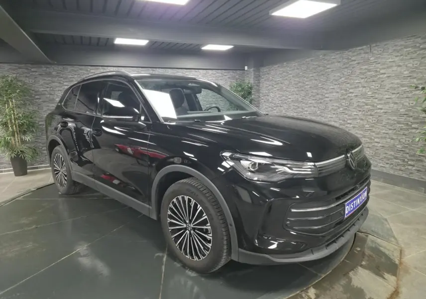 Volkswagen Tiguan noir en 3/4 avant droit, jantes alliage distinctives, stationné en intérieur moderne.