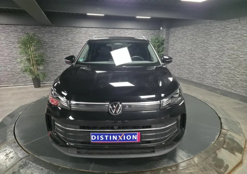 Vue avant d'un Volkswagen Tiguan noir 2025 avec calandre chromée et plaque Distinxion en intérieur showroom.