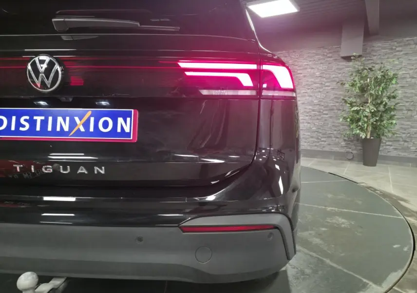 Vue arrière droite d’un Volkswagen Tiguan noir avec feux LED allumés et crochet d’attelage visible en showroom.