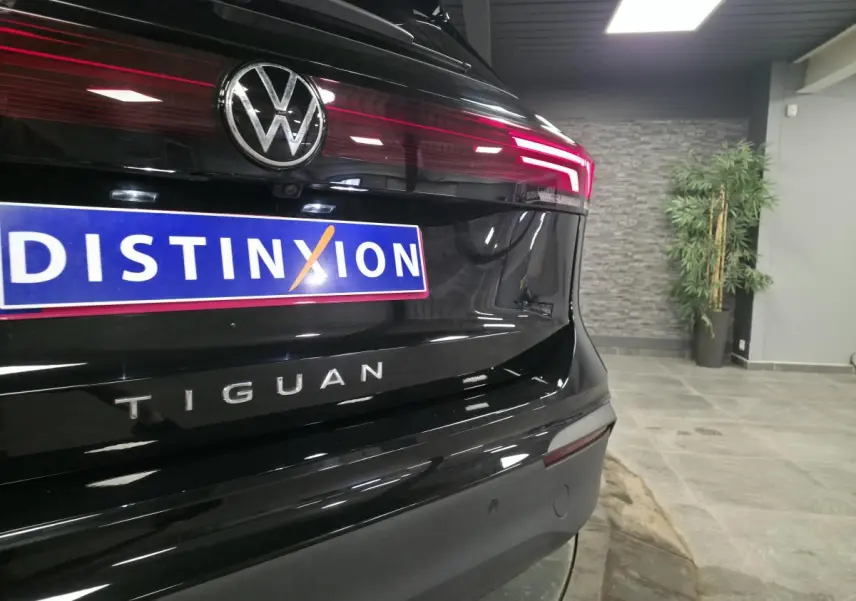Vue arrière rapprochée du Volkswagen Tiguan noir avec feux LED allumés et logo distinctif sur fond intérieur showroom.