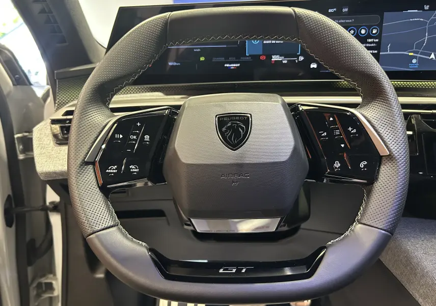 Vue rapprochée du volant cuir perforé du Peugeot 5008 Hybrid 2025 avec logo et commandes intégrées.