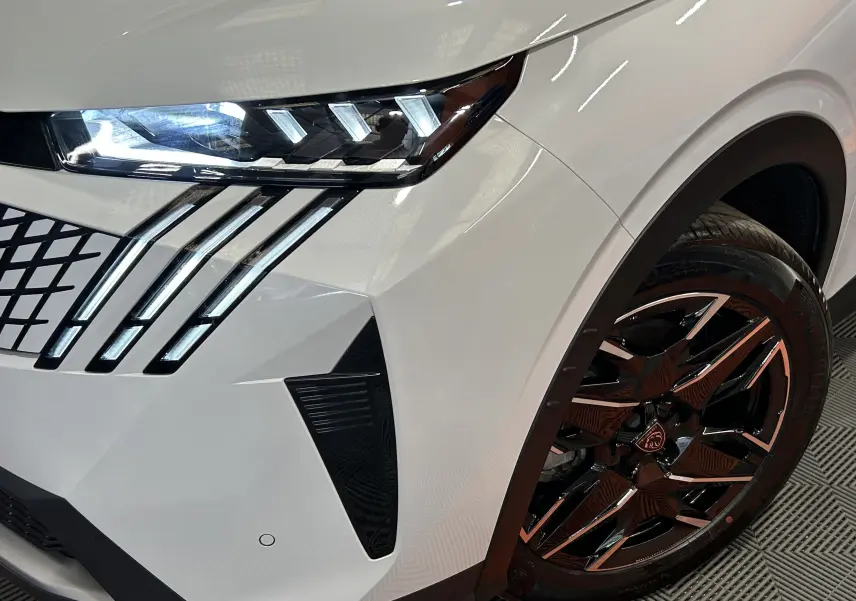 Gros plan sur l’avant droit blanc du Peugeot 5008 Hybrid 145ch GT, mettant en valeur les phares LED et la jante noire brillante.