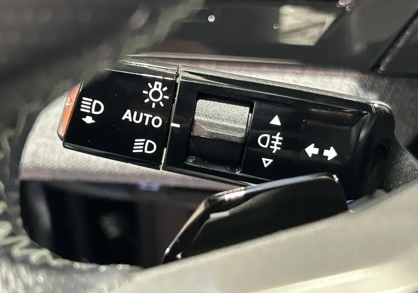 Gros plan sur la commande des phares et clignotants du Peugeot 5008 Hybrid blanc, côté gauche du volant.
