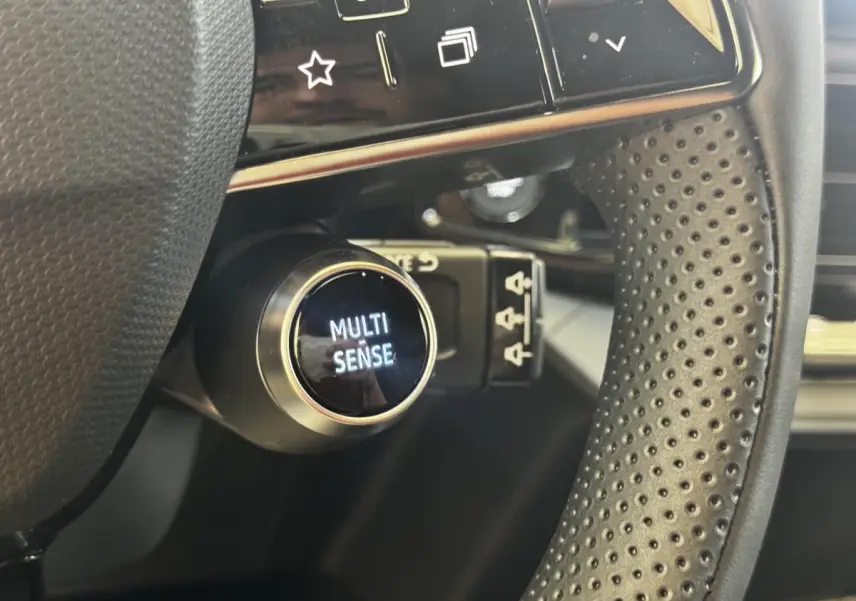 Gros plan sur le bouton Multi-Sense derrière le volant perforé du Renault Clio Techno TCe 115 essence 2026.