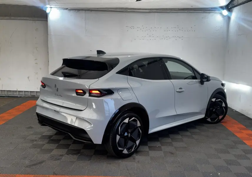 Vue 3/4 arrière droite d'une Renault Clio gris clair 2026 avec feux LED et jantes noires au design moderne.