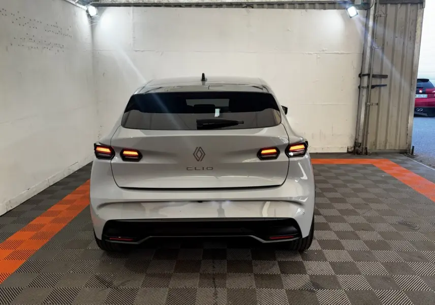Vue arrière d'une Renault Clio gris clair 2026 avec feux LED allumés, stationnée sur un sol à damiers gris et orange.
