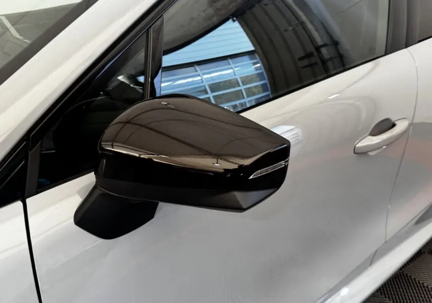 Rétroviseur droit noir brillant sur Renault Clio gris clair, vue rapprochée du côté avant droit.