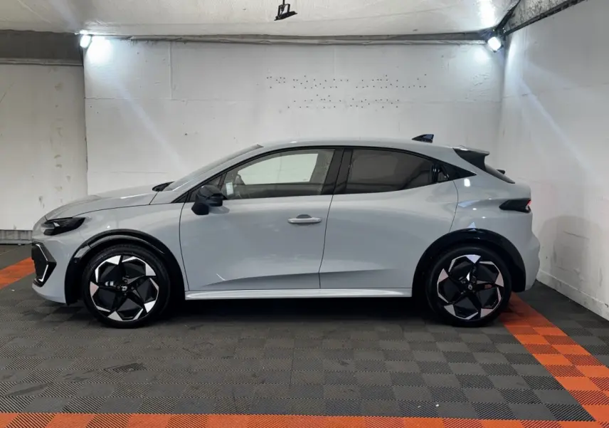 Profil droit d'une Renault Clio Techno gris clair, avec jantes noires et détails modernes en intérieur de garage.