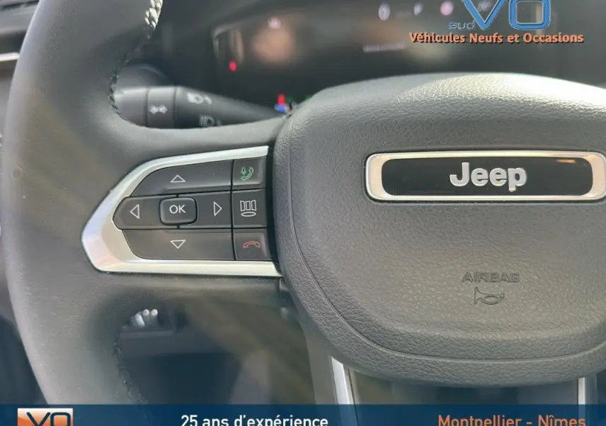 Gros plan sur le volant noir du Jeep Compass 2024 avec commandes intégrées et logo central visible.
