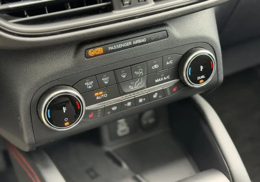 Gros plan sur la console centrale du Ford Kuga 2023, montrant les commandes de climatisation automatique bi-zone et sièges chauffants.